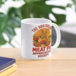 White ceramic mug printed with boxing kangaroo in gloves holding meat pie under orange outback sunset